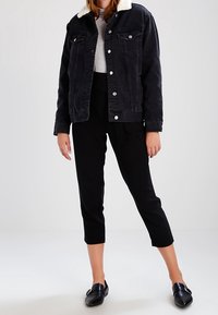 Svart denimjacka med en vit fuskpälskrage, två bröstfickor och silverknappar. Kombinerad med svarta korta byxor och svarta loafers.