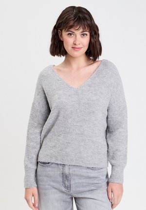 Grauer V-Ausschnitt-Pullover mit langen Ärmeln und lockerem Schnitt, hergestellt aus strukturiertem Strickmaterial. Gerippter Saum und Bündchen. Kombiniert mit hellen Jeans.