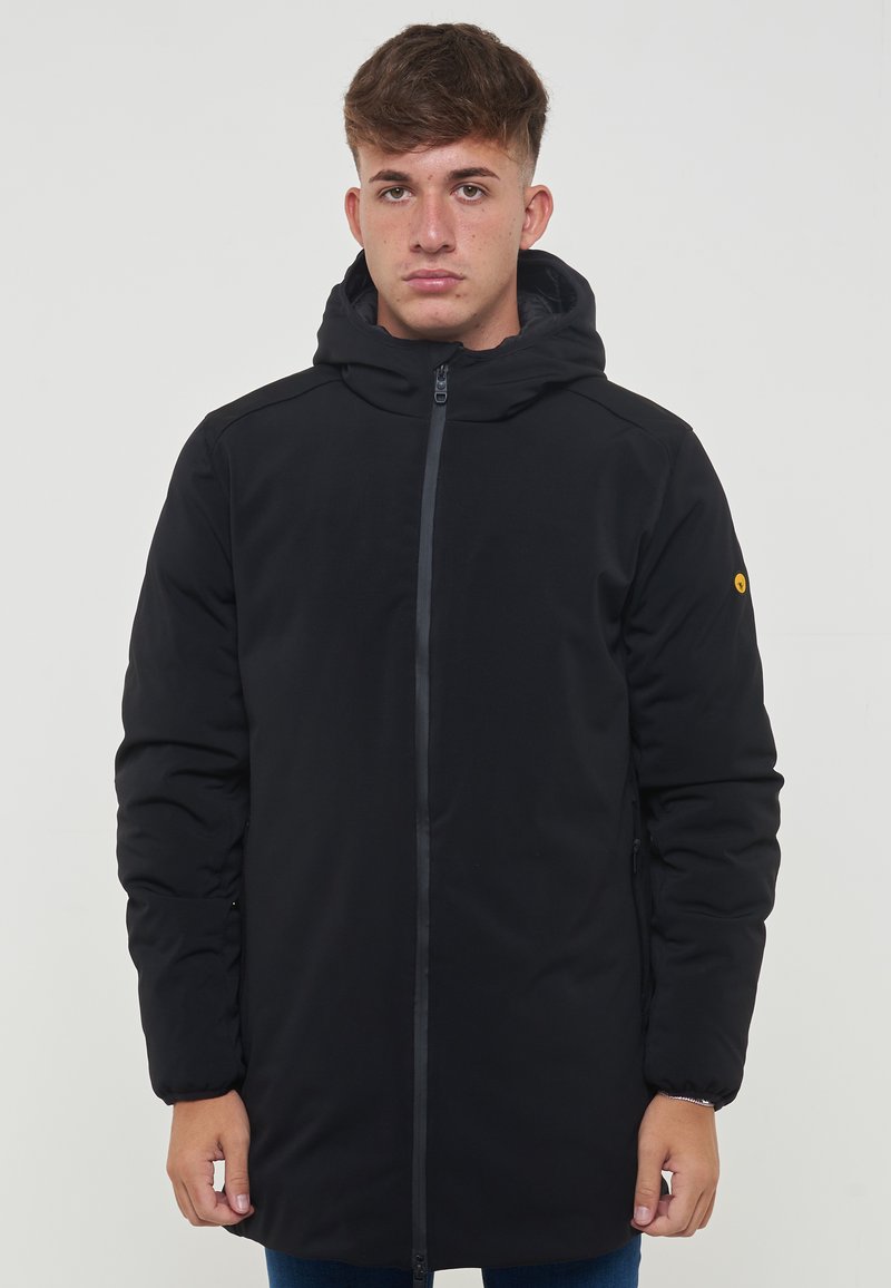 Parka nera imbottita con cappuccio, zip frontale eTaspringo. Dotata di un distintivo logo giallo sulla manica sinistra. Texture liscia.