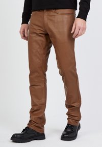 Braune Lederhosen mit schmaler Passform, glatter Textur und minimalen Nähdetails. Kombiniert mit schwarzen Schnürschuhen.