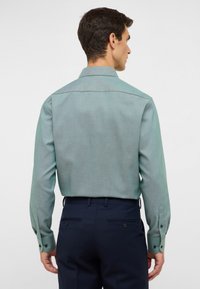 Lichtgroen gebloemd overhemd met lange mouwen, een klassieke kraag en knopenmanchetten. Draagt met een marineblauwe broek, met een getailleerde pasvorm.