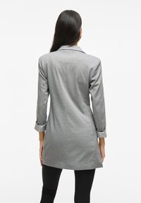 Cappotto grigio a maniche lunghe con vestibilità su misura, caratterizzato da polsini interni a strisce e un colletto elegante, realizzato in tessuto morbido con una leggera lucentezza.