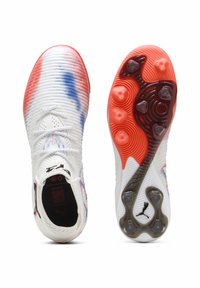 Scarpe da calcio con una tomaia bianca e testurizzata, accentuata da strisce rosse e blu. Presenta una suola con motivo e chiodi distintivi per una migliore aderenza.