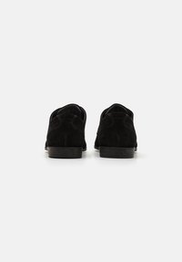 Chaussures en suede noir avec une texture lisse, un bout arrondi et un petit talon empilé. Présente des accents de couture et un design minimaliste.