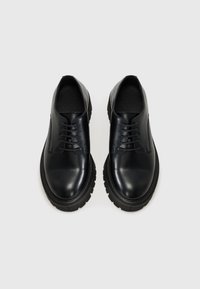 Chaussures en cuir noir à lacets avec une finition lisse, bout arrondi et semelle en caoutchouc épaisse dotée d'un motif de semelle texturé.