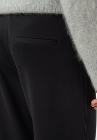 Czarne spodnie o eleganckim kroju z tylną kieszenią i gładką fakturą. Połączone z jasnoszarym, miękkim swetrem.