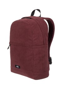 Sac à dos en velours côtelé bordeaux avec une texture lisse, de forme arrondie, une poignée supérieure et une poche zippée à l'avant. Dispose de bretelles rembourrées réglables.