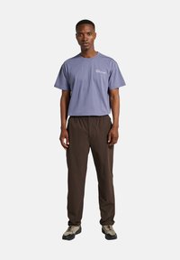 Paarse katoenen t-shirt met korte mouwen en een borstprint; bruine broek met elastische taille; grijze en zwarte sportschoenen met gestructureerde zolen.