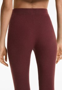 Burgunderfarbene, gerippte Leggings mit hohem Bund, strukturiertem Stoff und anliegendem Design, das vertikale Linien zeigt.
