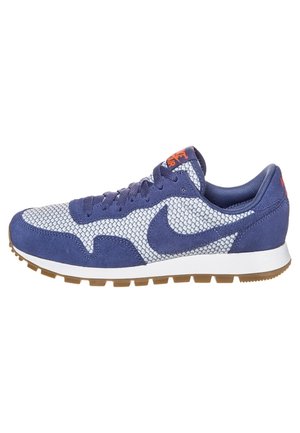 Chaussure de sport en suède et maille bleu marine avec une semelle intercalaire blanche et une semelle extérieure en caoutchouc brun. Présente un logo Nike bien en vue et des accents orange.
