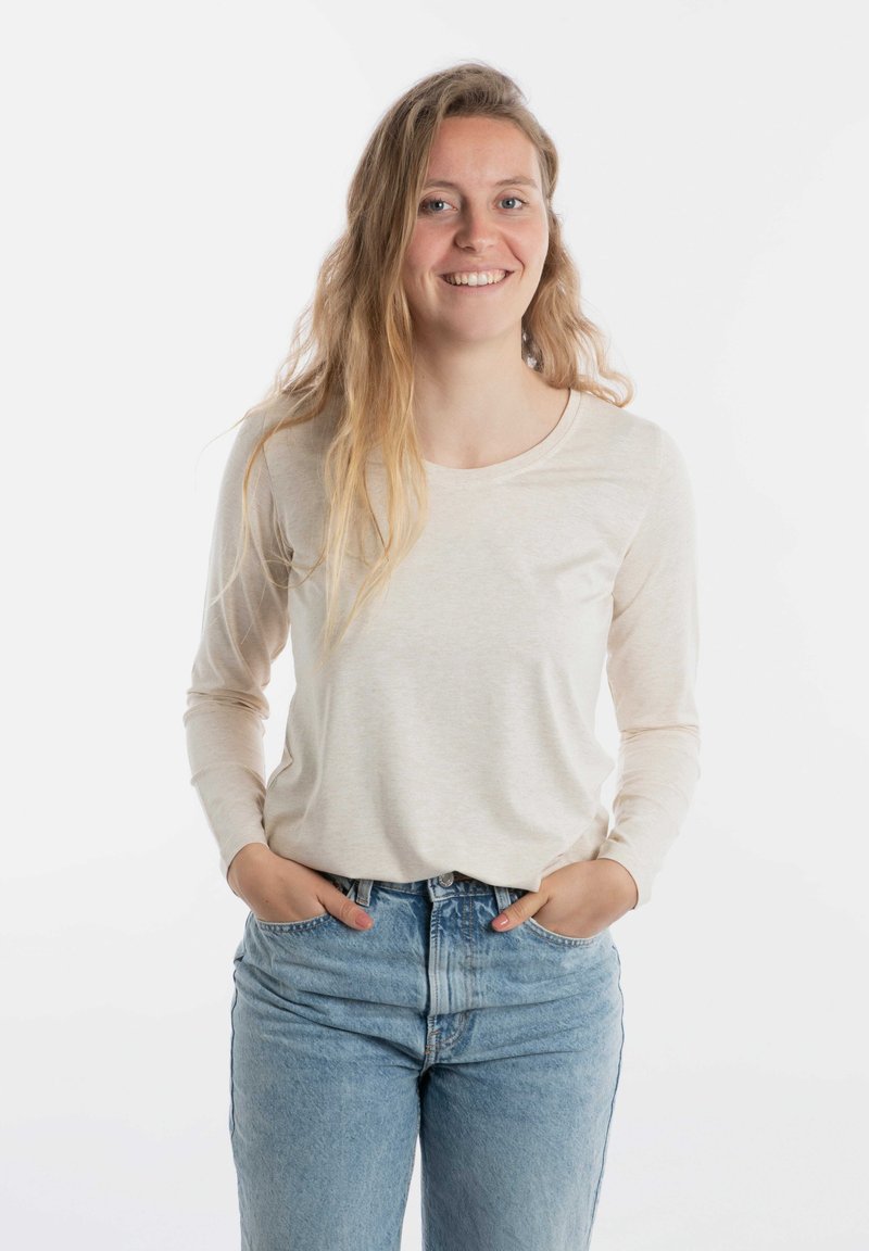 Lange mouwen, crèmekleurig shirt van zachte stof, met een ronde halslijn en een zak. Draag het met blauwe hooggewaist jeans.