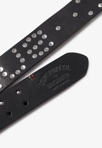 Sort læderbælte med metalnitter i et mønster, med en struktureret underside og præget branding på remmen.