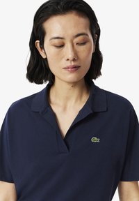 Mörkblå polo skjorta i strukturerad tyg med en tvåknapppslå och en liten grön krokodil-emblem på bröstet.