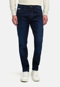 Dark blue denim jeans with a straight-leg cut, featuring contrast stitching, five pockets, and a single button closure. Paired with white sneakers.