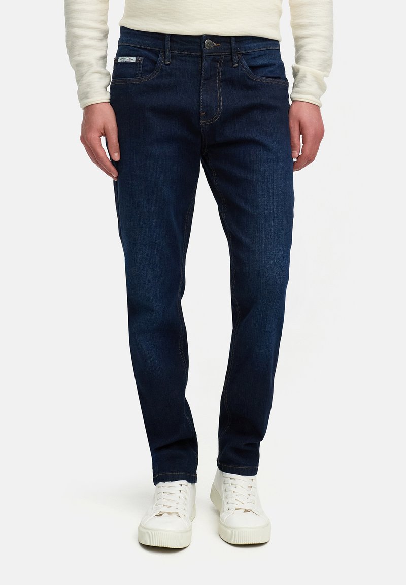 Dark blue denim jeans with a straight-leg cut, featuring contrast stitching, five pockets, and a single button closure. Paired with white sneakers.