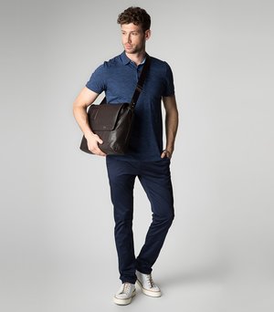 Borsa a tracolla in pelle marrone scuro con patta, tracolla regolabile e design elegante. Indossata da una persona in polo blu e pantaloni navy.