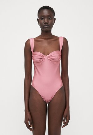 Bañador de una pieza en rosa suave, con tirantes anchos, detalle de escote fruncido y piernas de corte alto, fabricado con material suave.