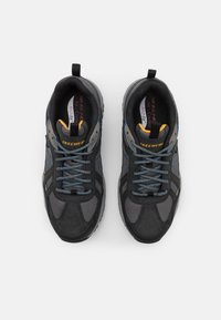 Černé a šedé sportovní boty s mesh panely a semišovými akcenty. Mají modré tkaničky a poutko. Logo "SKECHERS" na jazyku.