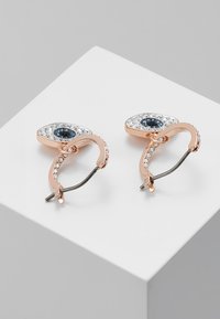 Øreringer i roségull med et øyeformet design med en sentral blå edelsten, omgitt av klare krystaller, og en teksturert spenne bak.