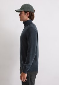 Pulover de culoare bleumarin închis, cu guler înalt, confecționat dintr-un material moale, având mâneci lungi și un design ajustat, completat cu o pălărie din catifea verde.