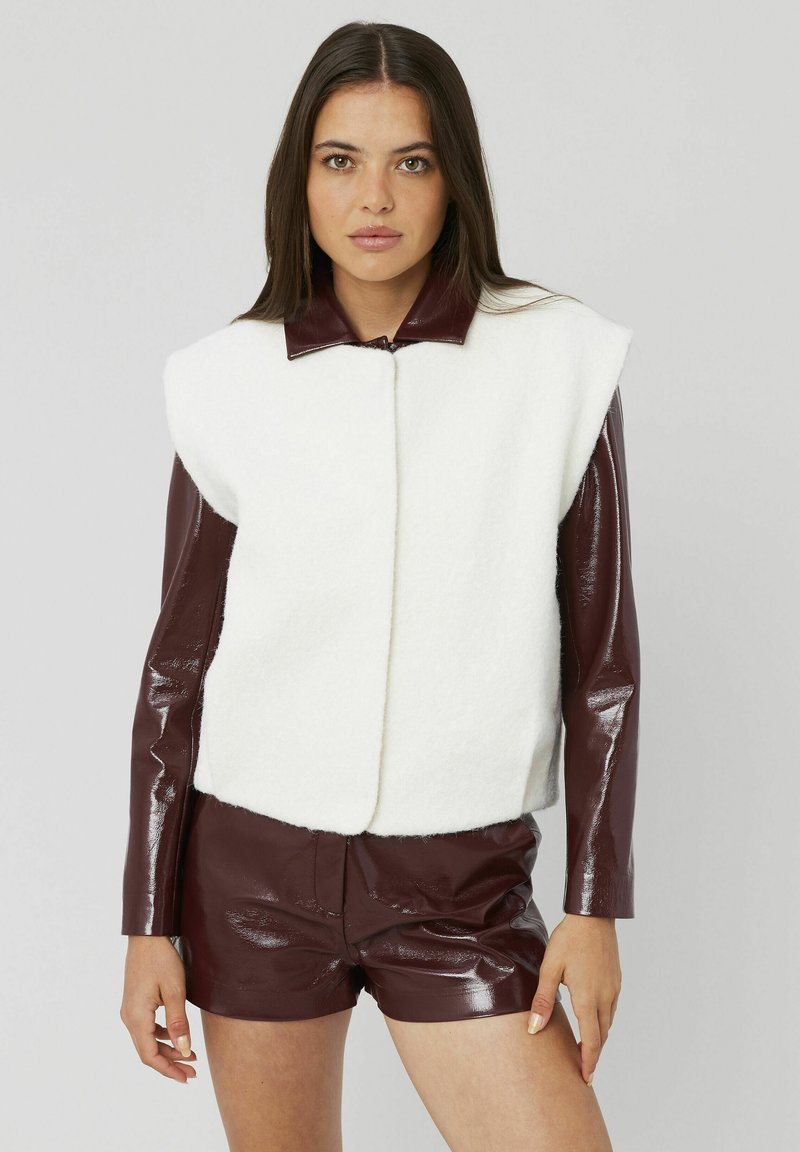 Gilet en peluche blanc avec col et manches en cuir bordeaux, associé à des shorts bordeaux brillants, mettant en avant un design moderne et structuré.