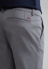 Pantaloni grigi in misto cotone con una texture liscia, dotati di una tasca posteriore con una piccola etichetta con la bandiera norvegese rossa e blu. Design slim fit.