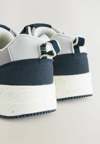 Des baskets avec une tige bleu marine et gris clair, en suède texturé et en mesh, une semelle blanche mouchetée et des languettes.