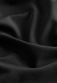 Sort stof med en glat, mat tekstur, der har subtile diagonale rilninger og draperede folder, der reflekterer lys i bløde skygger.