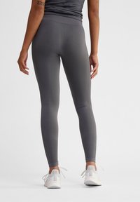 Grå leggings med en jämn yta, hög midja och subtila ribbade detaljer. Bärs med vita sportskor, sedd från baksidan.