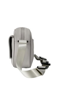 Bolso de bandolera compacto gris con una amplia correa ajustable y un bolsillo con solapa en el frente, mostrado de lado sobre un fondo blanco.