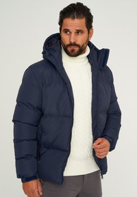 Marineblaue Steppjacke mit Reißverschluss, angenähter Kapuze und gerippten Bündchen. Verfügt über ein gestepptes Design und leicht glänzende Textur.