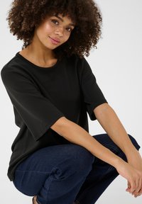 Svart överdimensionerad t-shirt med korta ärmar, rund halsringning, slät textur; kombinerad med mörkblå jeans.