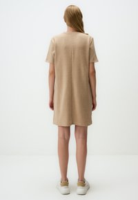 Beige Strickkleid mit kurzen Ärmeln, rundem Halsausschnitt und geradem Schnitt. Es hat eine Naht auf der Rückseite und eine glatte Textur.