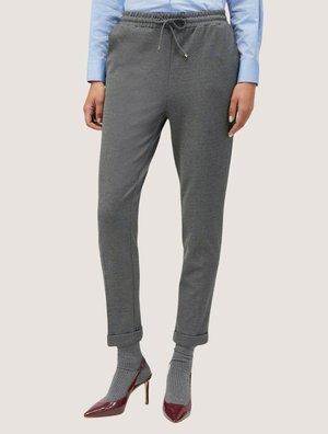 Grijze joggerbroeken met een trekkoord in de taille, met de broekspijpen opgerold bij de enkels, gecombineerd met grijze sokken en bordeauxrode hakken.