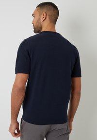 Suéter de punto corto de manga corta en azul marino con mangas de patrón texturizado, cuello redondo y dobladillo acanalado. Costuras planas y tejido transpirable.