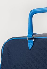 Saco azul-marinho com um padrão texturizado do nome da marca. Apresenta detalhes azuis suaves, uma forma estruturada e uma pega elevada com acabamentos metálicos.