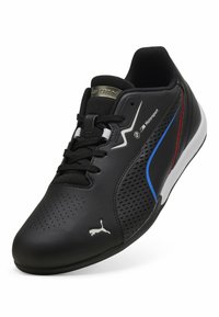 Baskets Puma Motorsport noires avec côtés perforés, accents bleus et rouges, logo blanc, et lacets noirs sur fond blanc.