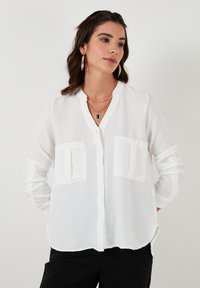 White button-up shirt with a mandarin collar, featuring two front pockets and rolled sleeves, made from a lightweight, textured fabric.