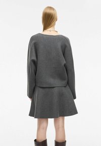 Sivi volneni pulover z ohlapnim krojem in spušenimi rameni, v kombinaciji z ujemajočo se krilom s širšo krojenjem. Gladka tekstura in preprost dizajn.