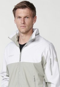 Veste légère avec un col haut, présentant une section supérieure blanche et une section inférieure grise. Comprend des poches zippées et un logo en relief.