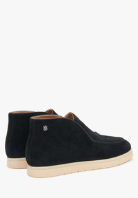 Zwarte suède instap-schoenen met een lage, crème-kleurige rubberen zool. Rond ontwerp met minimale stiksels en een kleine zilveren accent op de hak.