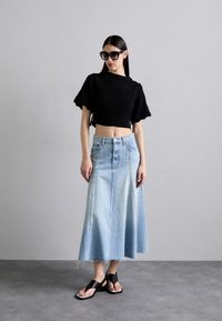 Pullover nero corto e texturizzato, gonna maxi in denim blu chiaro con orlo sfilacciato e sandali neri con cinturino trasparente.
