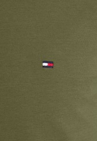 Olivegrünes Baumwoll-T-Shirt mit einem kleinen gestickten Logo in Blau, Weiß und Rot auf der Brust. Weiche, gestrickte Textur.