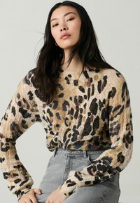 Beige gebreide trui met een luipaardprint in zwart, bruin en blauw. Lange mouwen met geribbelde manchetten; lichte en gestructureerde uitstraling.