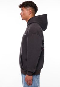 Dunkelgrauer Hoodie mit einer Fronttasche, verstellbarem Kapuzenrand und bedrucktem Text auf der Vorder- und Rückseite. Weiches Material aus Baumwollmischung.