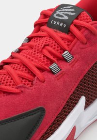 Red athletic shoes featuring a mesh upper, textured suede overlays, black accents, and a white sole with a red detail. "Curry" label on tongue.