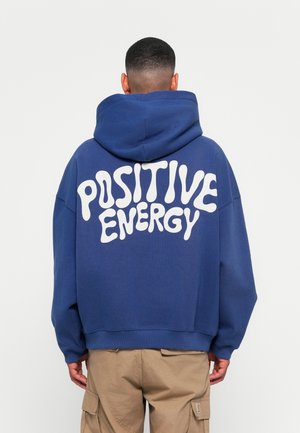Blue hooded sweatshirt featuring white, rounded lettering that says "POSITIVE ENERGY" on the back; relaxed fit with visible stitching details.