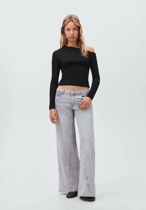 Haut noir à manches longues et épaules dénudées associé à un jean large gris clair. La tenue présente une silhouette ajustée et une texture en denim.