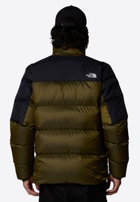 Puchowa kurtka w oliwkowo-zielonym kolorze z czarnymi ramionami. Posiada wysoki kołnierz oraz logo marki z tyłu. Teksturowana tkanina.