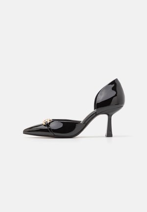 Schwarzer lacklederner High-Heel-Schuh mit spitzem Zehenbereich, rückenlosem Design, geschwungenem Absatz und goldenen Akzentdetails an der Vorderseite.